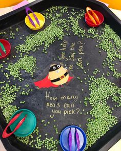 a black tray with green peas and plastic spoons on it that says how many peas can you pick?