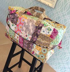 a multicolored bag sitting on top of a stool next to a wall with a mirror