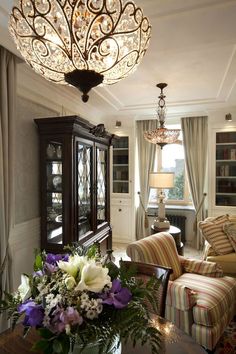 a living room filled with furniture and a chandelier hanging from the ceiling over a wooden table