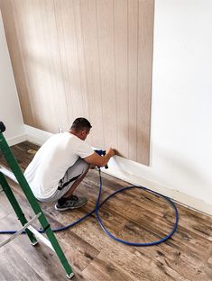 a man is using a hose to clean the floor in front of a wooden paneled wall