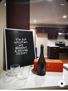 a bottle of beer sitting on top of a counter next to two glasses and a sign