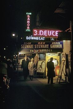 people walking down the sidewalk at night in front of a 3 d deuce store