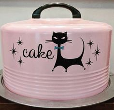 a pink cake tin with a black cat on it's side and the words cake written in large letters