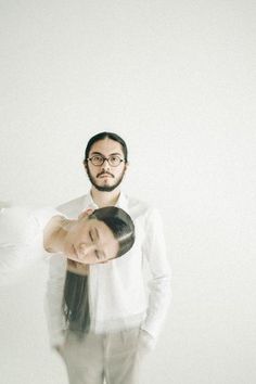 a man and woman standing next to each other in front of a white wall with one holding the other's head