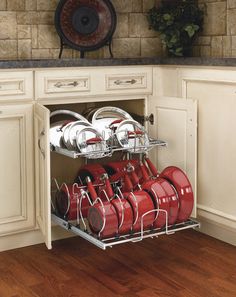 an open cabinet with red pots and pans in the bottom rack, on a wooden floor