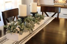 two candles are sitting on top of a white box with greenery and flowers in it