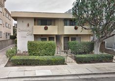 an apartment building with bushes and trees on the sidewalk