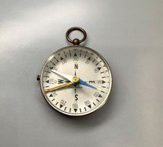 an old fashioned compass hanging on the side of a metal wall with blue and yellow hands