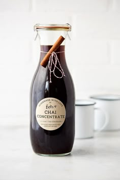 a glass bottle filled with liquid next to two mugs on a white counter top