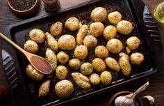 a pan filled with potatoes on top of a table next to garlic and seasoning