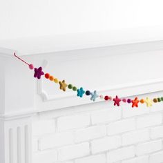 a string of colorful pom poms hanging from a white brick wall next to a fireplace