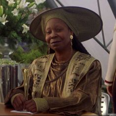 a woman sitting at a table wearing a hat and holding a pen in her hand