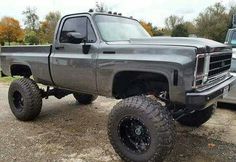 a large gray truck parked on top of a dirt road next to a silver truck