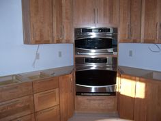 an empty kitchen with wooden cabinets and stainless steel oven in the center, along with white walls