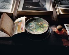 an open book sitting on top of a wooden table next to pictures and a bowl