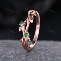 a rose shaped ring with green stones in the center on top of a stone surface