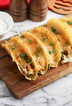 three tacos sitting on top of a wooden cutting board