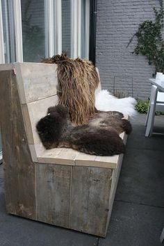 the cat is sleeping on the back of the wooden bench in front of the window