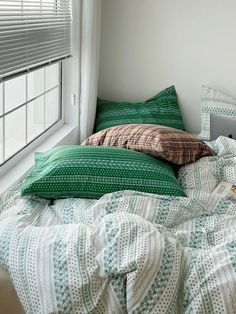 an unmade bed with green and white sheets in front of a window on a sunny day