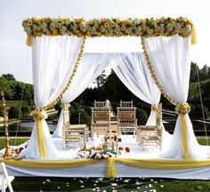 an outdoor wedding set up with white drapes and yellow sashes on the ground