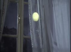 a yellow tennis ball sitting on top of a window sill next to a curtain