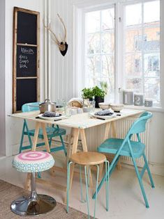 a kitchen table with four chairs and a chalkboard on the wall behind it in front of a window