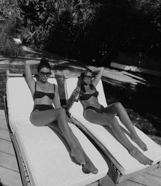 two women in bathing suits sitting on loungers by the water with their legs up