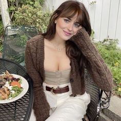 a woman sitting at an outdoor table with a plate of food in front of her