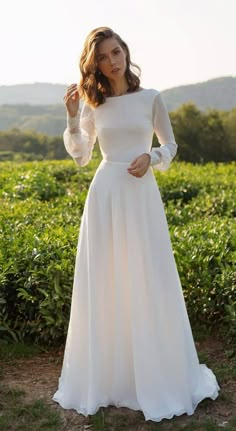 a woman wearing a white dress standing in the grass with her hands on her hips