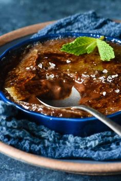 a blue bowl filled with food on top of a wooden plate next to a spoon