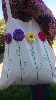 a woman holding a white bag with crocheted flowers on it