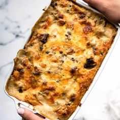 a person holding a casserole dish in their hand on a marble countertop