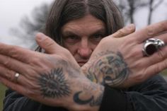 a man with long hair and tattoos holding his hands together