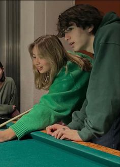 three people sitting at a pool table and one is holding a cue in her hand