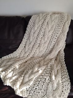 a white knitted blanket sitting on top of a leather couch