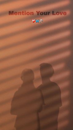 the shadow of two people standing next to each other in front of a wall with words written on it