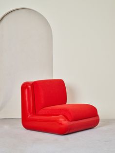 a red chair sitting in front of a white wall with a round mirror behind it