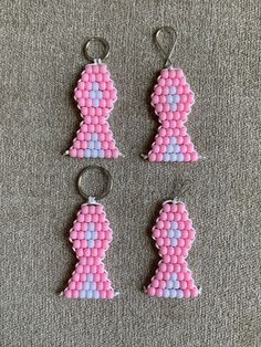 three pieces of pink and blue beaded earrings on a gray carpeted surface, with one piece shaped like a woman's head in the shape of a ribbon