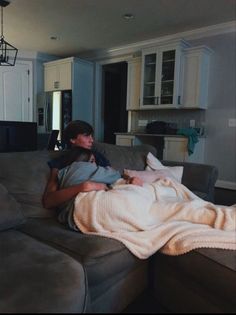 two people sitting on a couch with a blanket over their heads and one person holding a baby