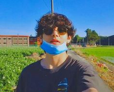 a young man wearing sunglasses and a neck gaiter in front of a green field