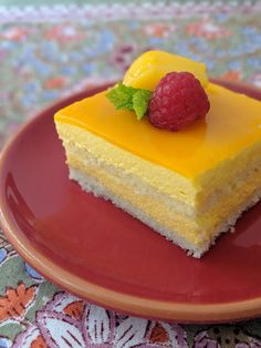 a piece of yellow cake with raspberries on top sits on a red plate