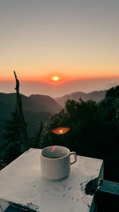 a coffee cup sitting on top of a white table next to a mountain at sunset