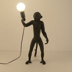 a black monkey lamp with a light bulb on it's head and hands holding the cord