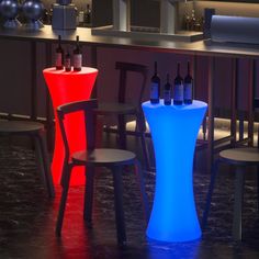 three stools and two tables with bottles on them in a room that is lit up at night