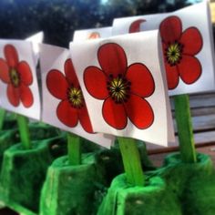 four red flowers are placed on top of each other in small green vases with sticks sticking out of them