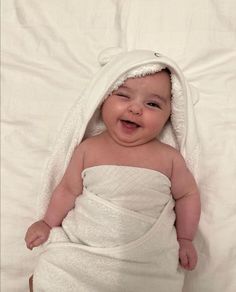 a smiling baby wrapped in a towel on top of a white sheet with his eyes closed