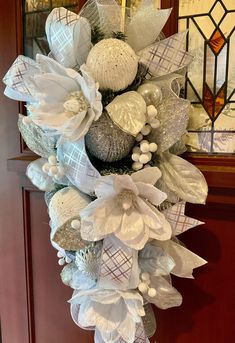 a wreath with white and silver decorations hanging from it's side on a door