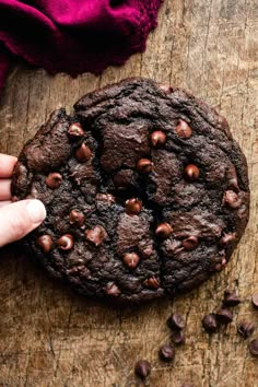 a person holding a chocolate cookie on top of a wooden table with chocolate chips around it