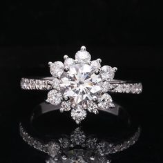 an engagement ring with a flower design on the side and round brilliant diamonds surrounding it