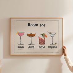 a person holding up a framed poster with different cocktails on it's wall